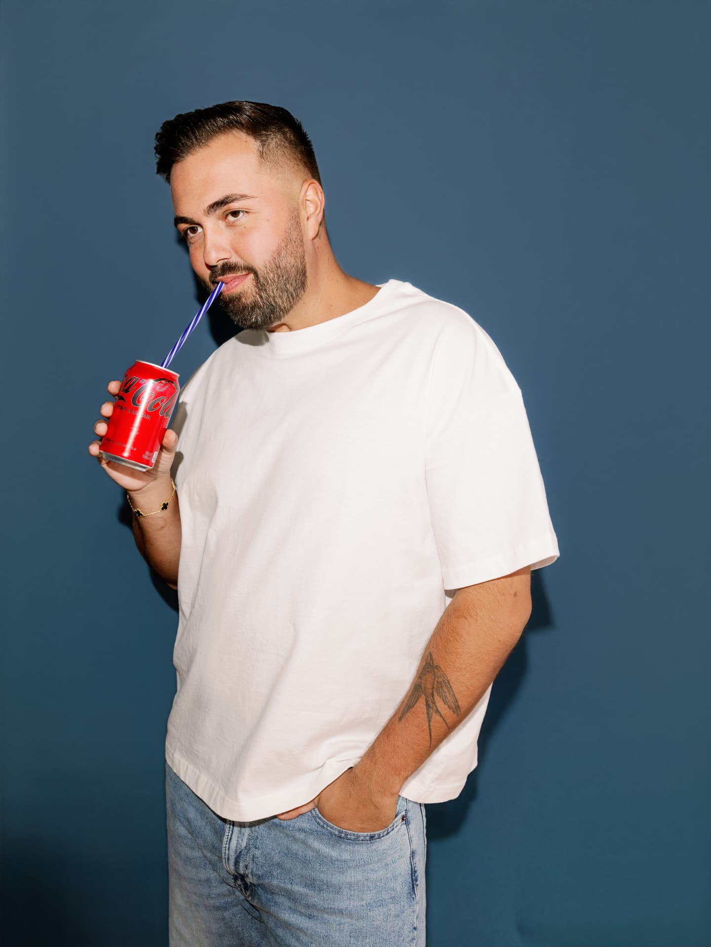 Dom C sipping a soda against a blue backdrop
