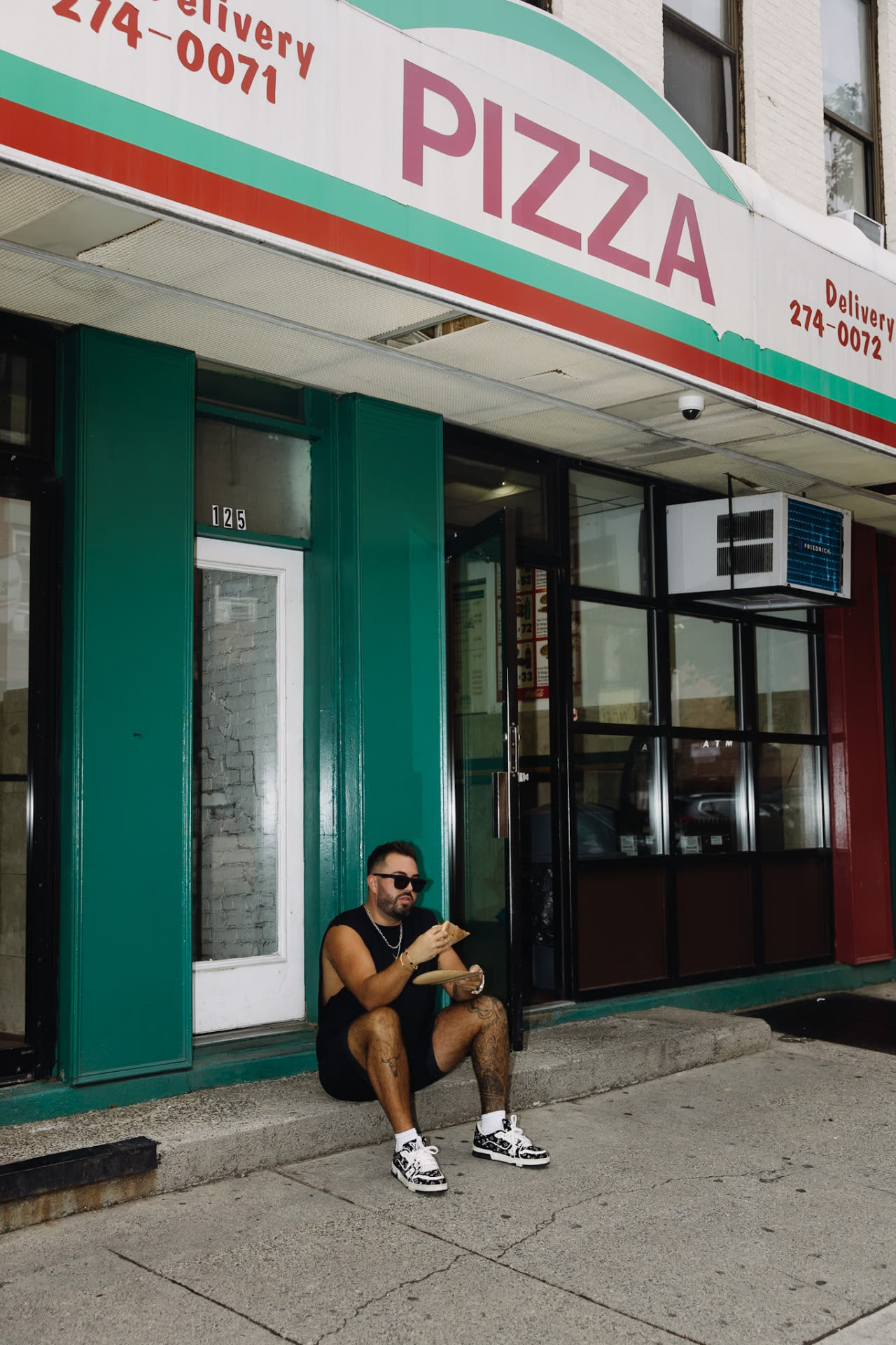 Dom C sitting outside a neighborhood pizza shop storefront