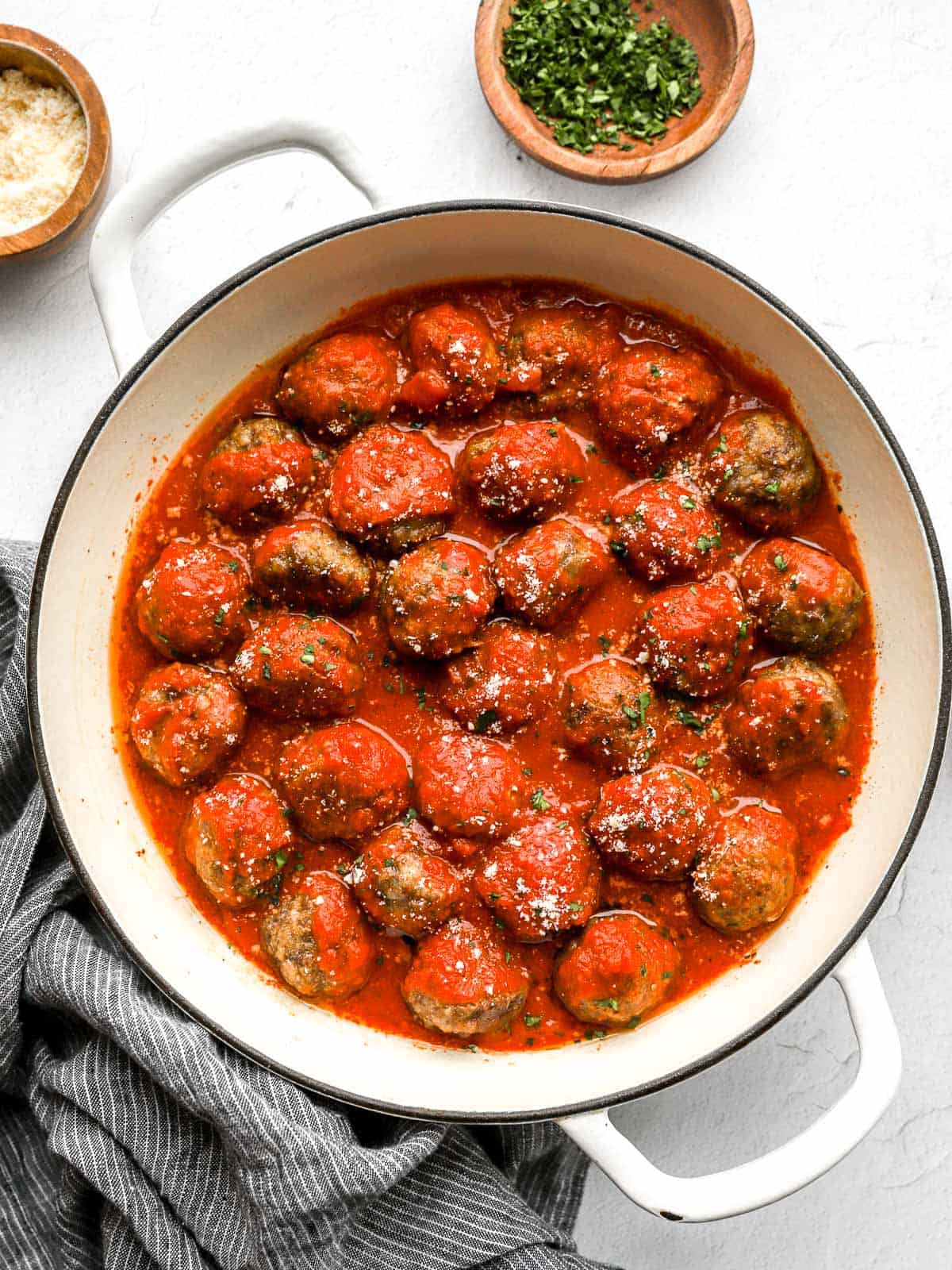 A pot of Mario's meatballs simmering in marinara with grated parmesan on top